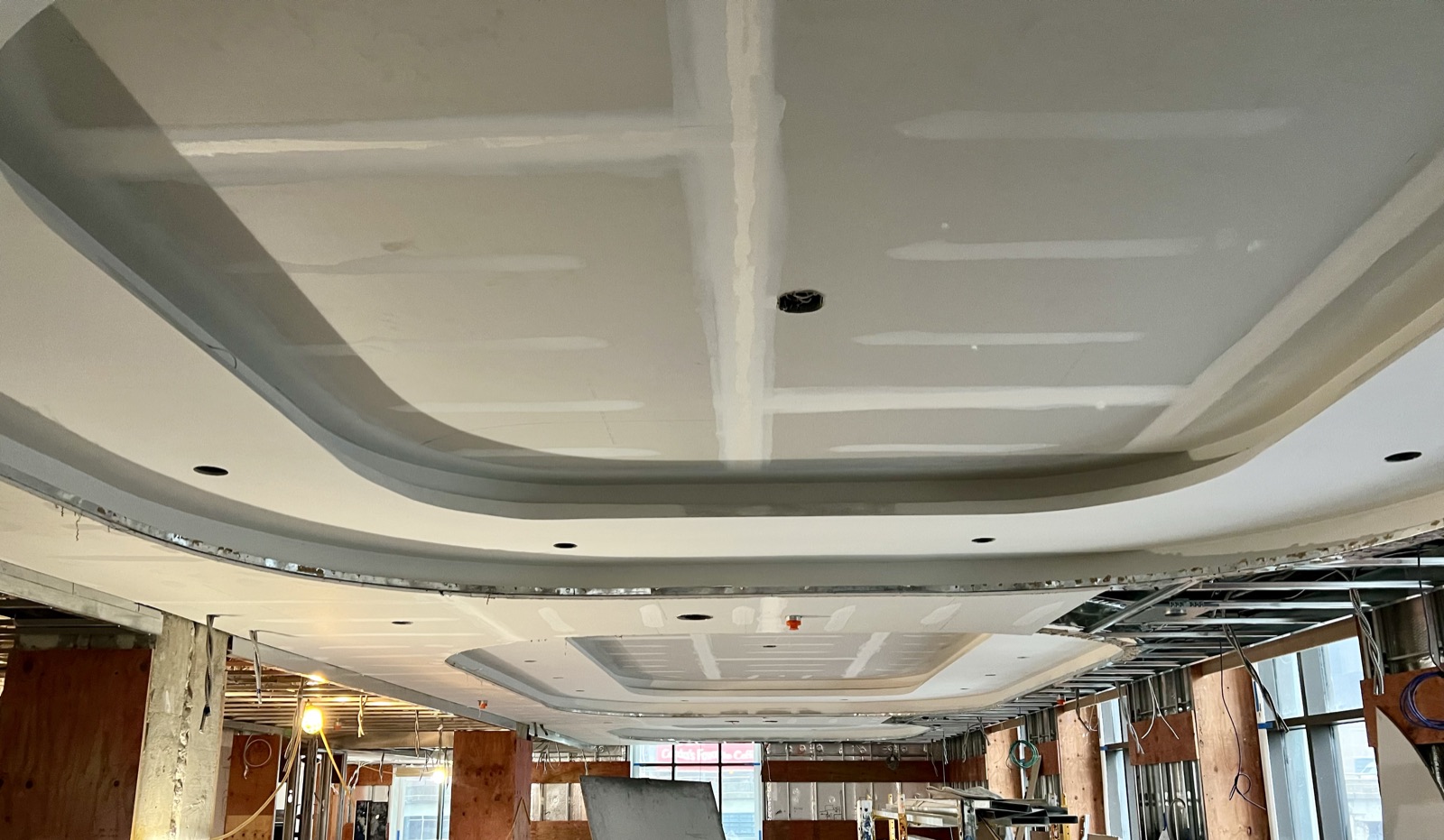 Curved bulkhead ceiling taped and mudded in a bright commercial space with floor-to-ceiling windows